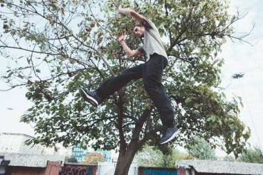 Spor elbiseli genç atletik adam dışarıda egzersiz yapıyor parka atlıyor.