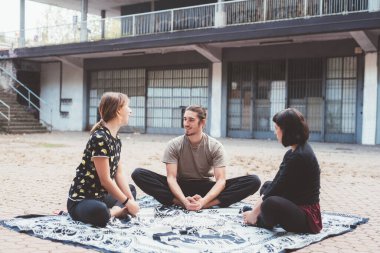 Dışarıda sabah antrenmanı yapan üç arkadaş yoga egzersizi yapıyor.