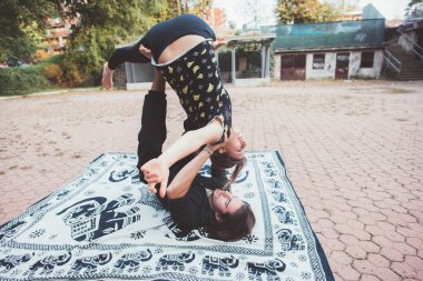 Healthy young man lying floor and balancing woman doing acrobatic yoga stretching exercise in the garden