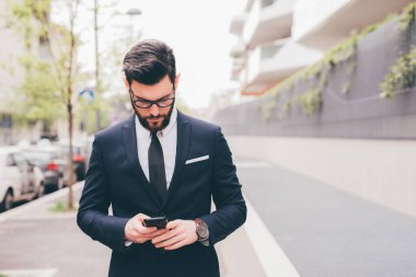 Young bearded elegant businessman outdoors using smartphone