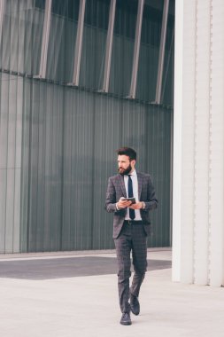 Young bearded elegant businessman wallking outdoors using smartphone