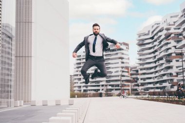 Enerjik, genç, sakallı profesyonel iş adamı havada zıplıyor.