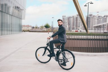 Zarif sakallı, genç ve şık bir iş adamı bisikletle işe gidip karbondan arınmış bir şekilde işe gidiyor.