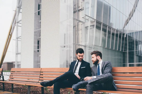 Two Young Elegant Businessmen Sitting Outdoors Bench Discussing Chatting — Stock Photo, Image