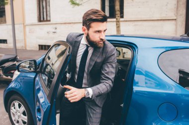 Young bearded elegant businessman opening the car door to exit