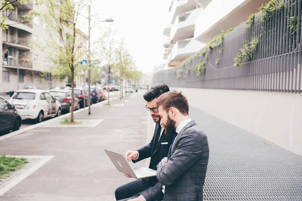 Two Businessman Sitting Outdoors Business District Using Sharing Netbook Computer — Photo