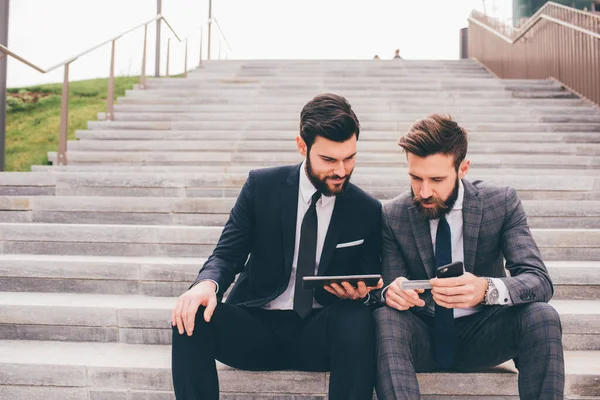 Two Businessman Sitting Outdoors Staircase Using Sharing Tablet Smartphone Discussing — Stock Fotó