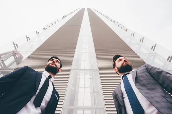 背の高いビジネスビルに対する2人の現代的な白人ひげそりのビジネスマンの低角度ビュー — ストック写真