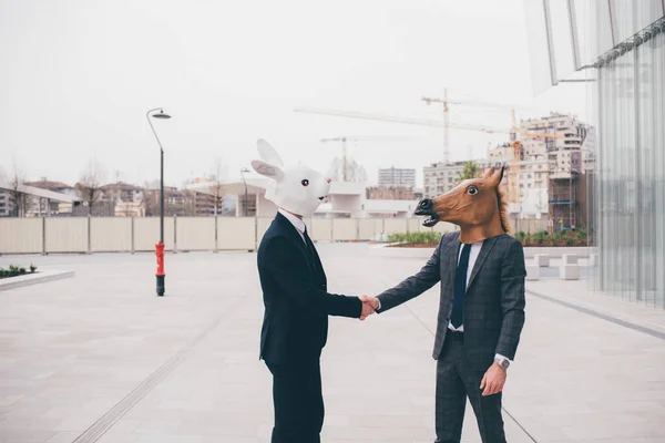 两个戴面具的当代商人在高层办公大楼前握手 狂欢节 神圣的 奇怪的概念 — 图库照片