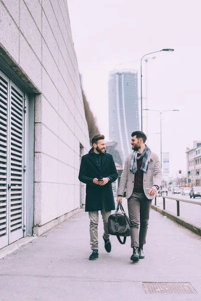 2人の若いビジネスマンがスマートフォンを使って屋外を歩き — ストック写真