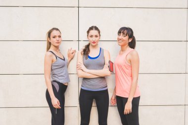 Şehirde eşofman giyen, kameraya bakıp gülümseyen, spor, mutluluk, egzersiz konsepti olan üç güzel beyaz kadın.