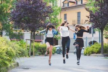 Şehirde üç genç kadın koşuyor ve zıplıyor, gülüyor ve eğleniyorlar.