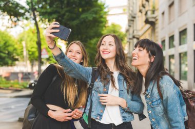 Üç genç kadın akıllı telefonla selfie çekiyorlar.