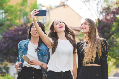 Üç genç kadın akıllı telefonla selfie çekiyorlar.