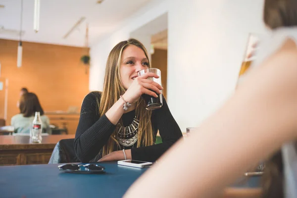 2人の若い女性が屋内に座ってバーでしゃべり ソフトドリンクを飲みながら話す — ストック写真