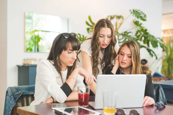 Three young millennials women indoor using computer discussing