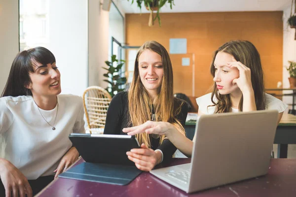 Three young millennials women indoor using computer discussing