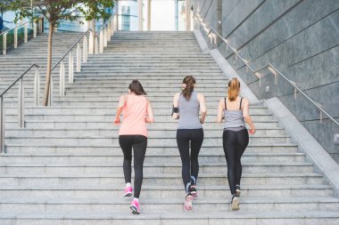 Üç genç ve sportif kadın üst kata koşuyor.