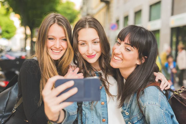 三位千禧年的年轻女性拿着智能手机自拍 — 图库照片