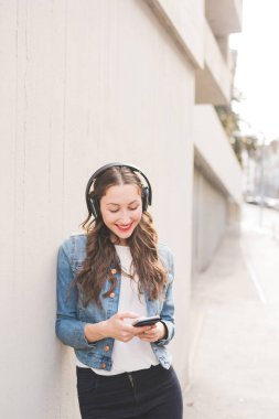 Genç bayan milenyum kuşağı açık havada akıllı telefon kullanarak müzik dinliyor.