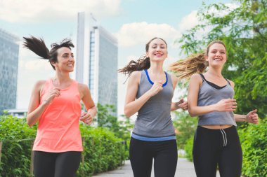 Üç genç sportif kadın açık havada antrenman yapıyor.