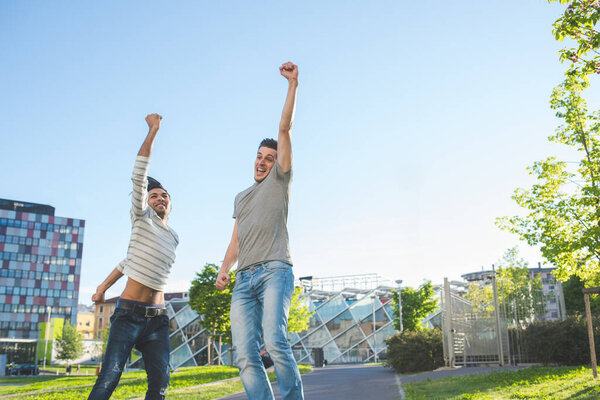 Два молодых мультиэтнических мужчины на открытом воздухе прыгают праздновать победу