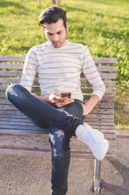 Genç adam dışarıda banka otururken akıllı telefon kullanıyor. 