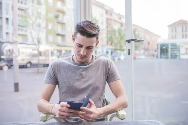 Młody Człowiek Pomocą Smartfona Siedzi Bar Zewnątrz — Zdjęcie stockowe
