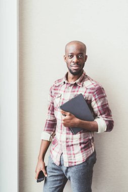 Tablet tutan genç bir iş adamı ve kapalı ofiste çalışan akıllı bir telefon.