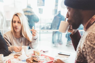 Üç çok ırklı arkadaş oturmuş kahvaltı yapıyorlar.