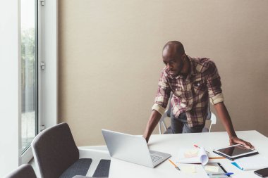 Genç siyahi adam ofis içinde dizüstü bilgisayar kullanıyor. 