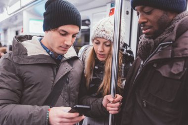 Üç kişi genç çoklu etnik gruplar halinde akıllı telefon kullanarak yeraltında seyahat ediyorlar. 