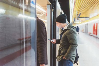 Genç, beyaz, güzel bir adam akıllı telefon kullanarak yer altında seyahat ediyor. Ekommerce, teknoloji, seyahat kavramı.