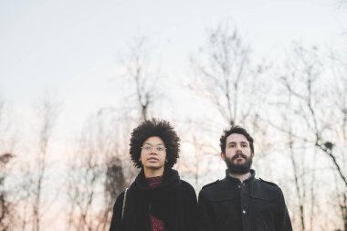 Gün batımında şehir sokaklarında poz veren çok ırklı genç bir çift.