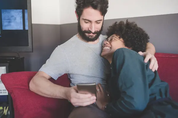 Pasangan Multietnis Muda Menggunakan Ponsel Pintar Dalam Ruangan Duduk Sofa — Stok Foto