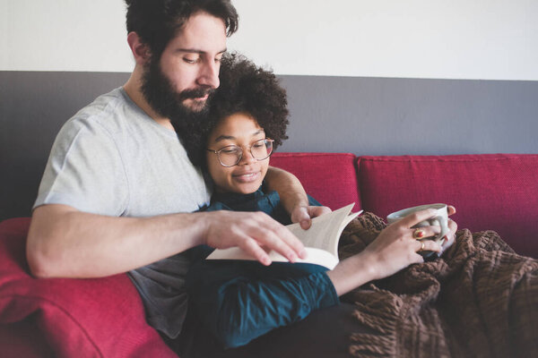 Young multiethnic couple hugging couch reading book 