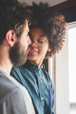 Genç, etnik çeşitlilikte bir çift evde gülümsüyor. 