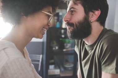 Genç, etnik çeşitlilikte bir çift evde gülümsüyor. 