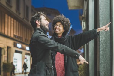 Geceleri çok ırklı genç bir çift dükkanın camına bakıp gülümsüyor ve alışveriş yapıyor.
