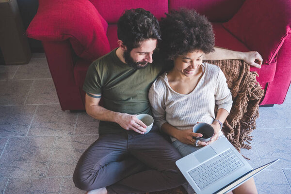 young multiethnic couple indoor watching streaming on computer having coffee 