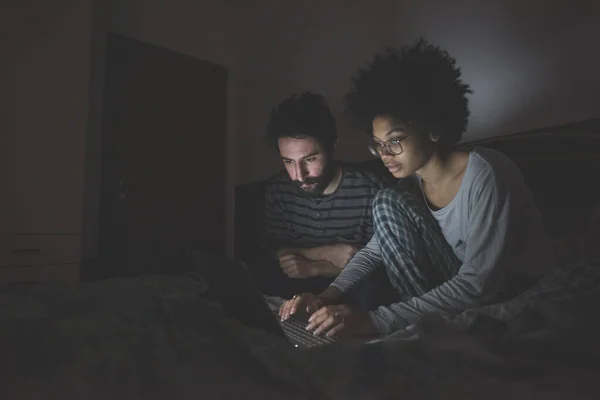 Pasangan Muda Multietnis Dalam Ruangan Menggunakan Komputer Berbaring Tidur Malam Stok Foto Bebas Royalti