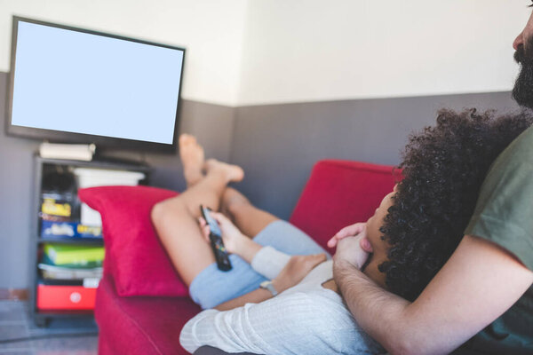 молодая многонациональная пара в закрытой квартире сидит диван смотреть телевизор