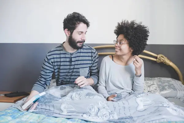 Jong Multi Etnische Paar Bed Met Behulp Van Smartphone Lezen Stockfoto