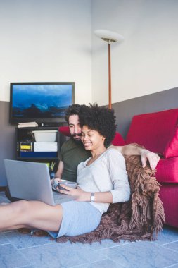 Genç, etnik çeşitlilikte bir çift bilgisayarda kahve içerken izliyorlar. 