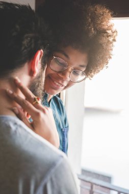 Çok ırklı genç çift gülümsüyor. Evlerinde birbirlerine sarılıyorlar.
