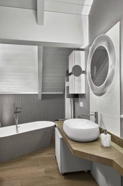 Ön planda modern bir banyo manzarası, arka plandaki ahşap tavan arası lavabosu küvet.