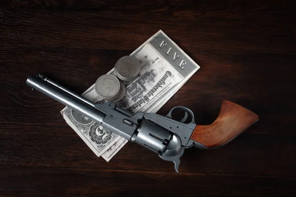 Old west revolver with bill and silver dollars on wooden table