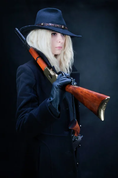 old west blonde girl wearing black hat with gun on black background
