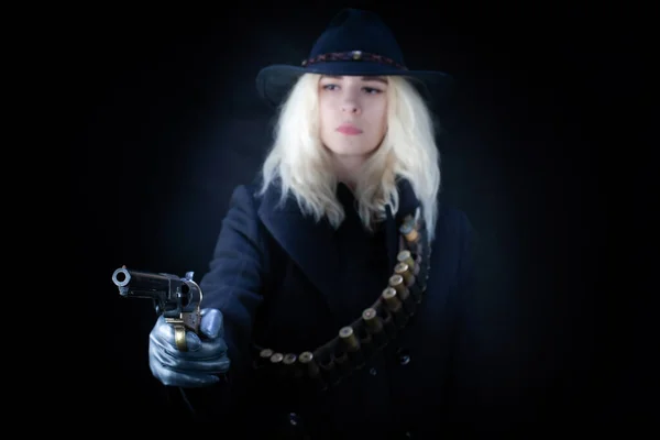 Old west blonde girl wearing black hat with revolver handgun on black background