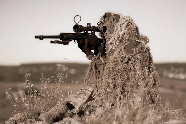岩の多い砂漠の丘の上の戦闘位置に光学スコープを備えた高精度のライフルでギリースーツの特殊部隊狙撃手 — ストック写真